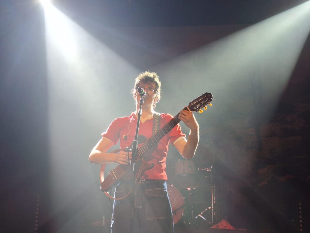 O vocalista da banda O Grilo aparece ao centro tocando em um show