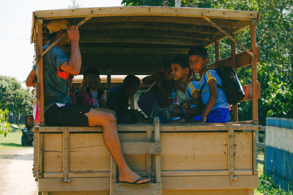 Crianças dentro de um veículo aberto, conversando entre si, uma delas olhando para fora, todas com uniforme, possivelmente em direção ou na saída da escola na Reserva Extrativista