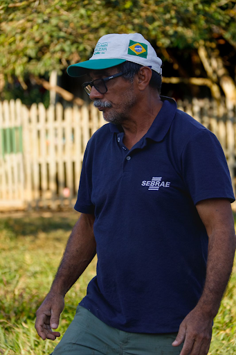 Imagem do líder da reserva extrativista Cazumbá-Iracema, com uma camisa do SEBRAE, um boné do Brasil e uma cerca desfocada no fundo da imagem