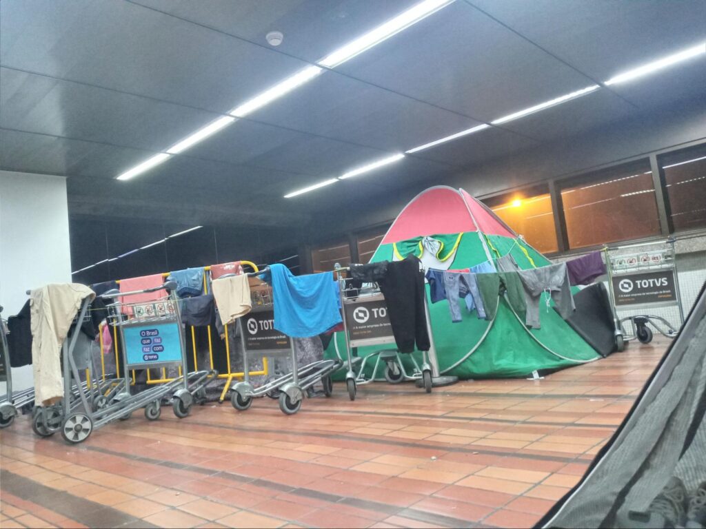 Carros de bagagem com roubas estendidas ao lado de uma barraca nas cores verde e vermelha.