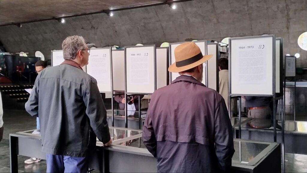 Dois homens em pé olham para fotos de edições anteriores do jornal O Politécnico