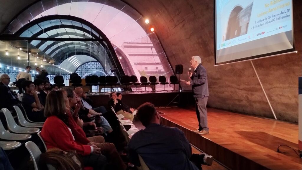 Homem discursa em palco para plateia que acompanha evento dos 80 anos de O Politécnico