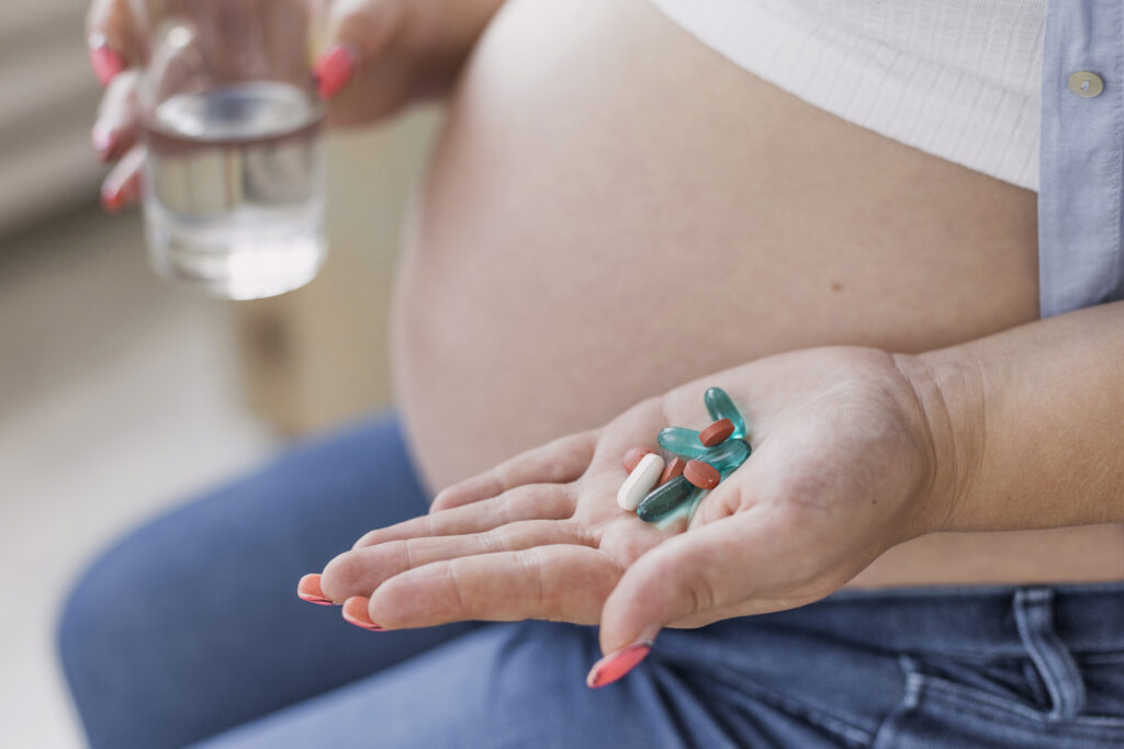 Mulher grávida segurando comprimidos em uma mão e um copo de água na outra