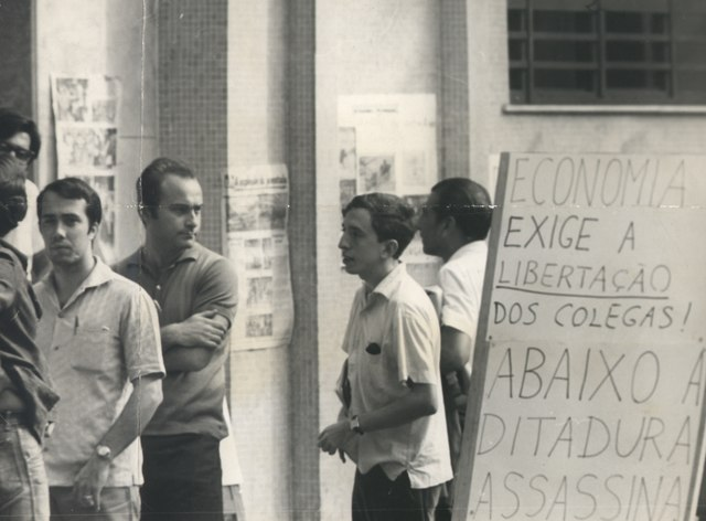 Pessoas ao lado de cartaz que critica a ditadura militar