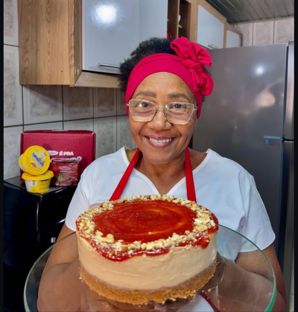 Eliete, do perfil Receitass de Vó, segura um doce que se assemelha a uma torta.