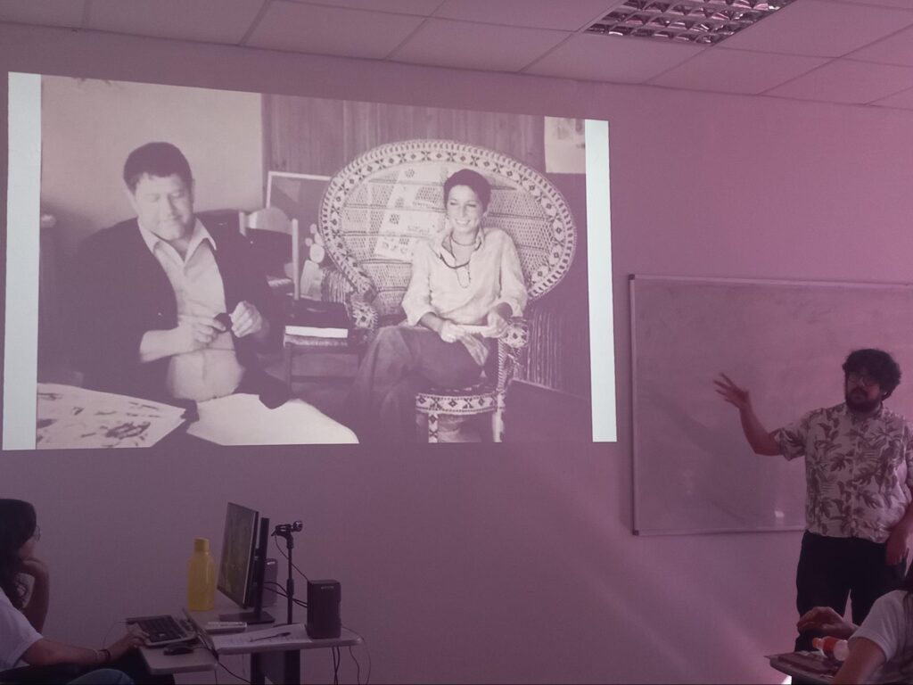 Fotografia apresentada durante o evento. Nela há uma mulher sentada em uma cadeira com encosto arredondado e um homem ao seu olho, que olha para o chão