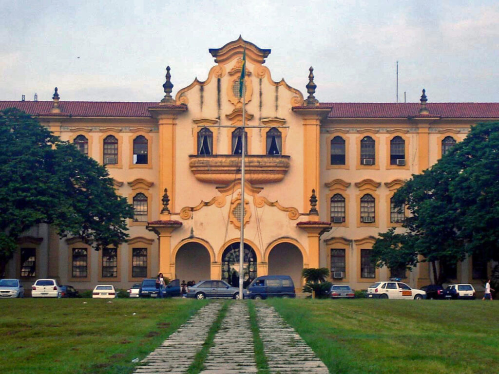 Fotografia do prédio principal da Universidade Federal Rural do Rio de Janeiro. Ele é amarelo e possui detalhes neocoloniais. Há um gramado na frente da construção.