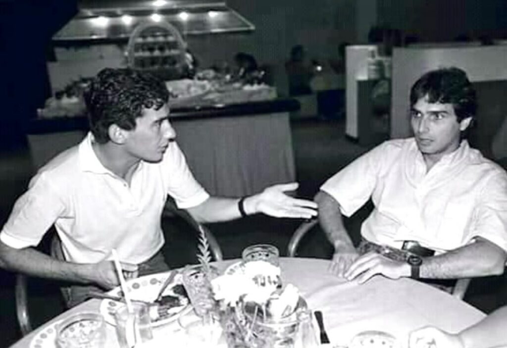 Nelson Piquet e Ayrton Senna conversando, sentados em uma mesa de jantar