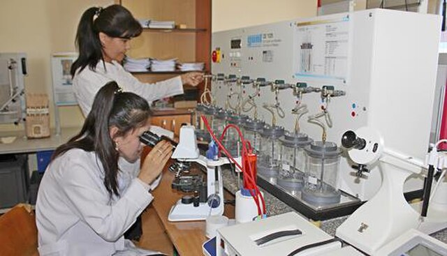 Duas cientistas realizando trabalho em laboratório, utilizando amostras e microscópio óptico