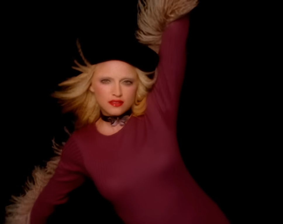 Madonna posa para foto. Ela usa um vestido justo na cor bordô, batom vermelho e uma boina preta. 