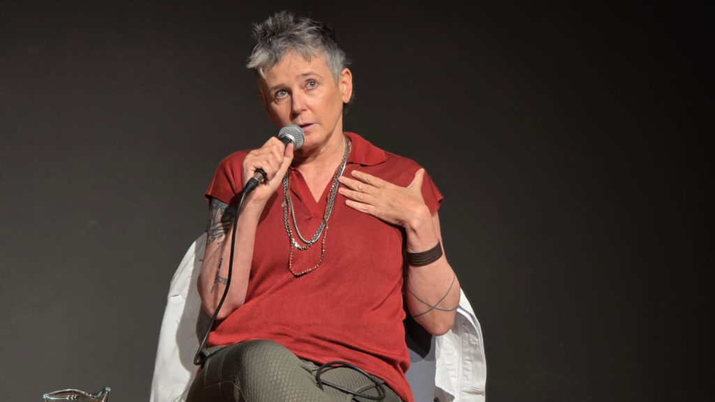 Milly Lacombe sentada. Ela olha em direção à foto 