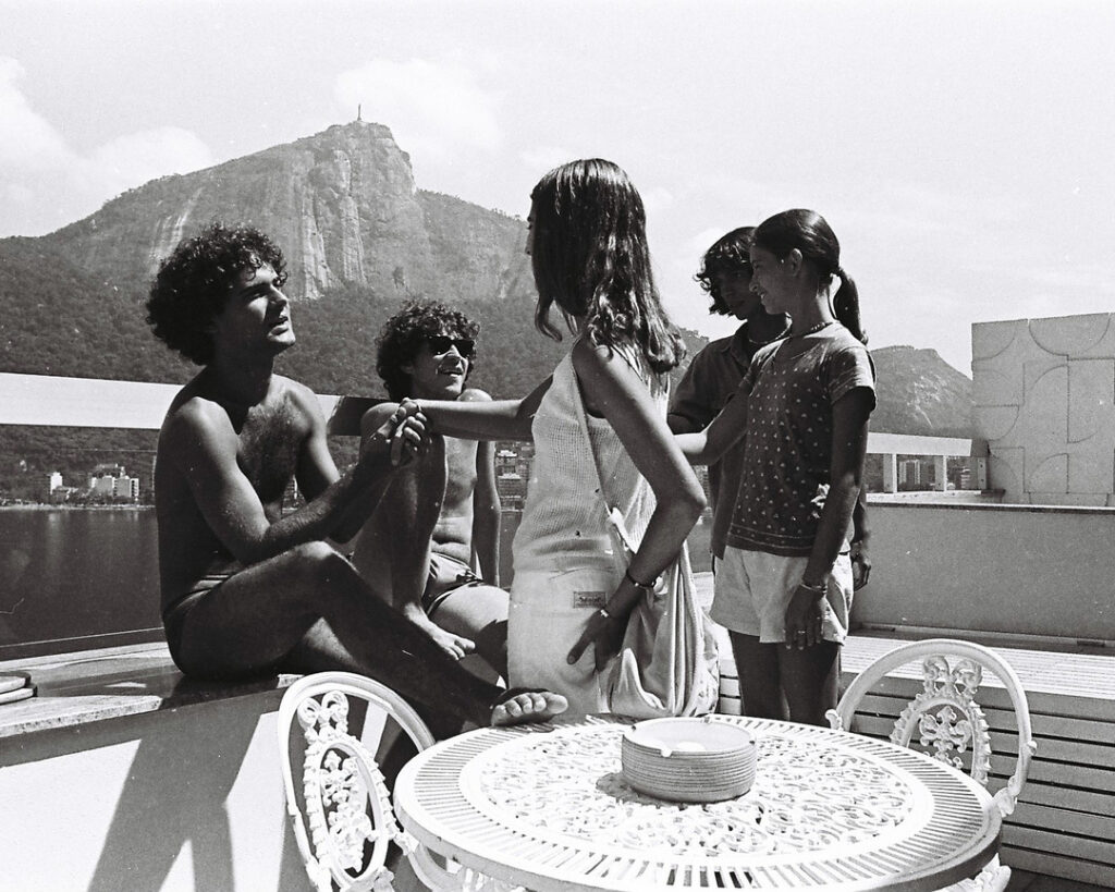 Cazuza na juventude, ao lago de amigos. Ele está sentado em uma mureta e a fotografia está em preto e branco.