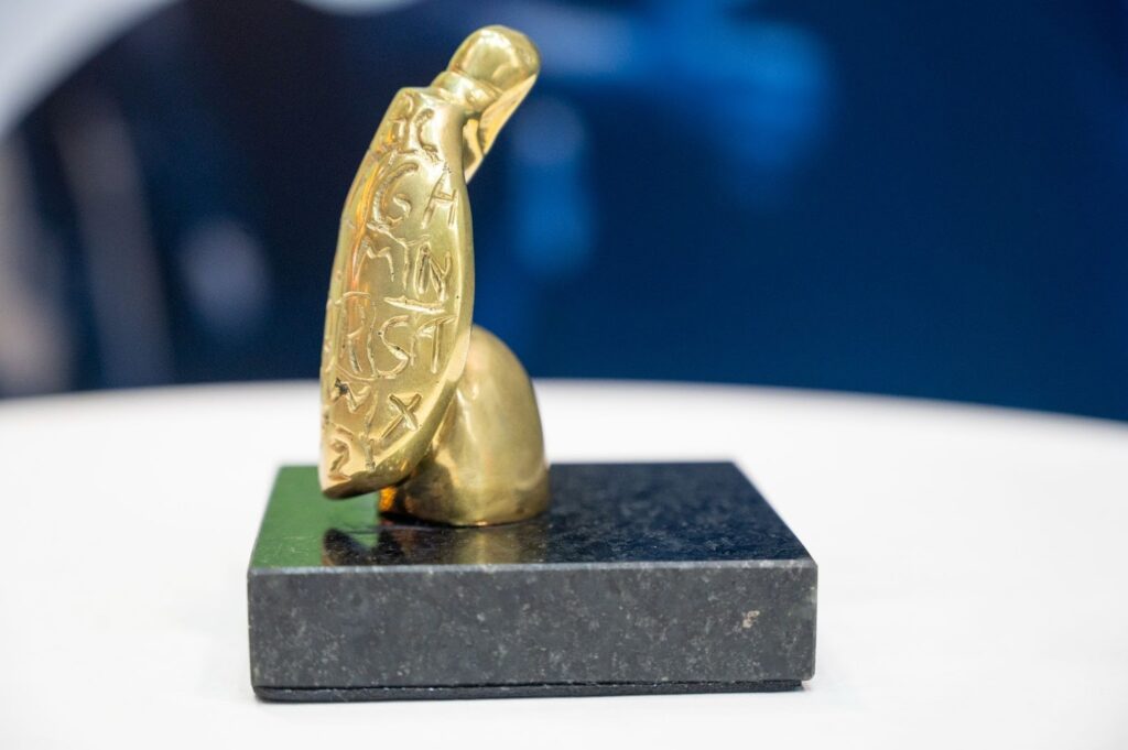 A imagem mostra a estatueta do prêmio que consiste em um jabuti dourado que apresenta letras do alfabeto em seu casco