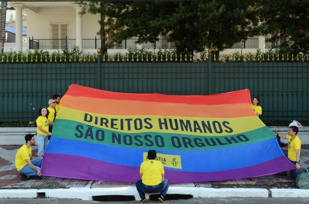 Pessoas segurando a bandeira LGBTQIA+ com os dizeres "Direitos humanos são nosso orgulho"