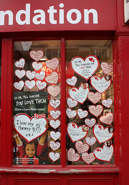Janela de uma loja da British Heart Foundation decorada com corações de papel que contém mensagens de amor escritas neles