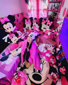 A imagem mostra Cleo da Silva situada em um recinto recheado de imagens da Minnie. Diversas pelúcias a rodeiam, bem como lençóis e tapetes possuem a face da personagfem estampada. Cleo está ajoelhada e sorrtindo para foto vestindo roupas estampadas com a personagem