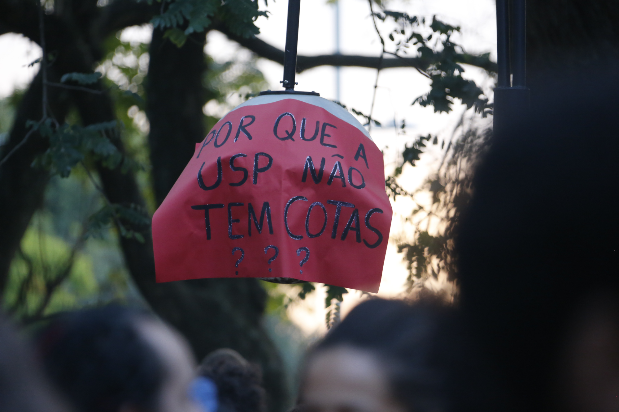 Na imagem, uma mão segurando um cartaz com os dizeres "Por que a USP não tem Cotas?"