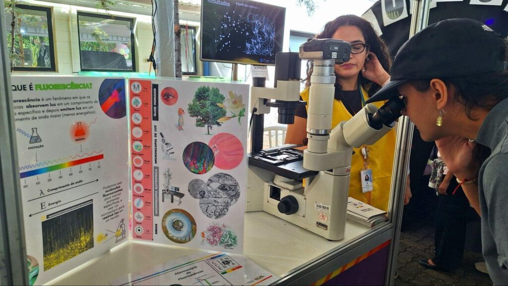 Mulher observa microscópio em mesa de exposição no CNPEM.