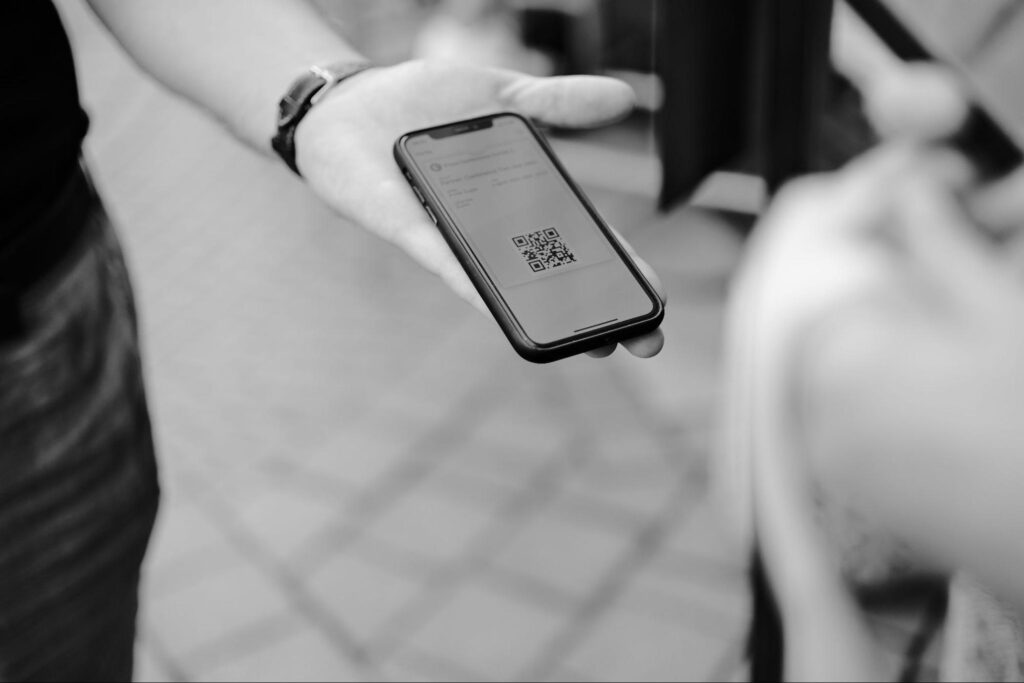 Foto em preto e branco com uma mão segundo um celular com QR code