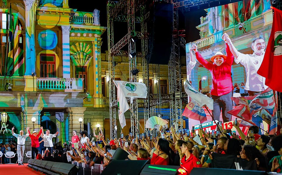 Multidão segurando bandeiras vermelhas em frente a um palco