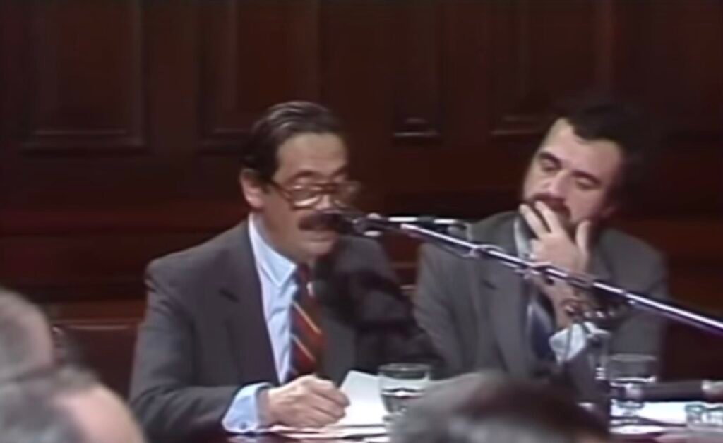 Dois homens brancos de terno cinza falando ao microfone