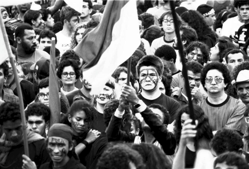 Pessoas em foto preto e branco num protesto segurando bandeiras e com símbolos hippies
