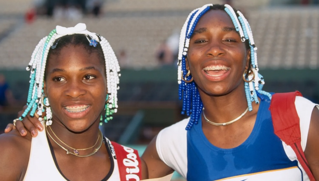 Serena e Venus Williams sorrindo com cabelos decorados com miçangas