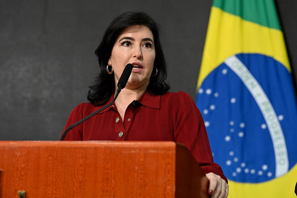 Mulher branca de camisa vermelha falando ao microfone