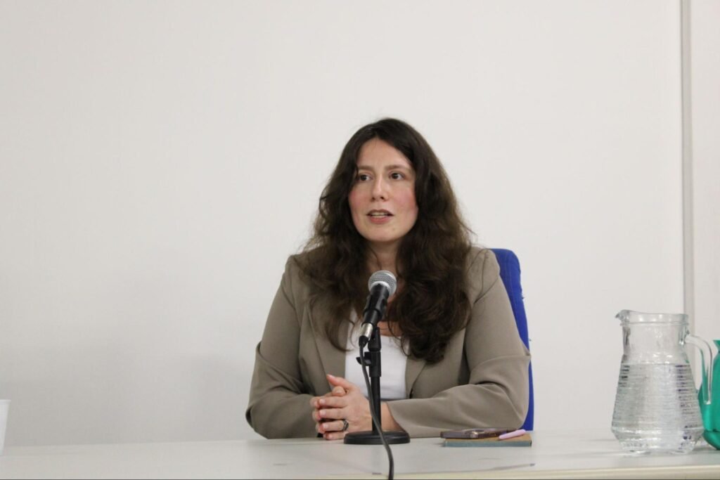 Mulher branca de blazer cinza falando ao microfone