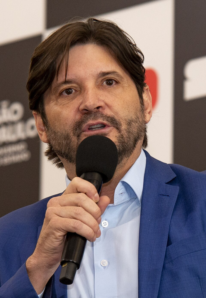 Homem branco de terno azul falando no microfone