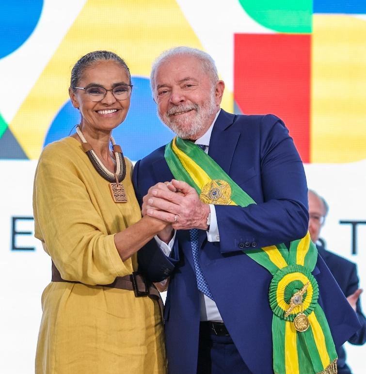 Mulher negra de óculos e roupa amarela com homem branco de terno azul e faixa presidencial