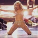 Britney Spears performando ajoelhada no palco com figurino de pedrarias nos anos 2000.