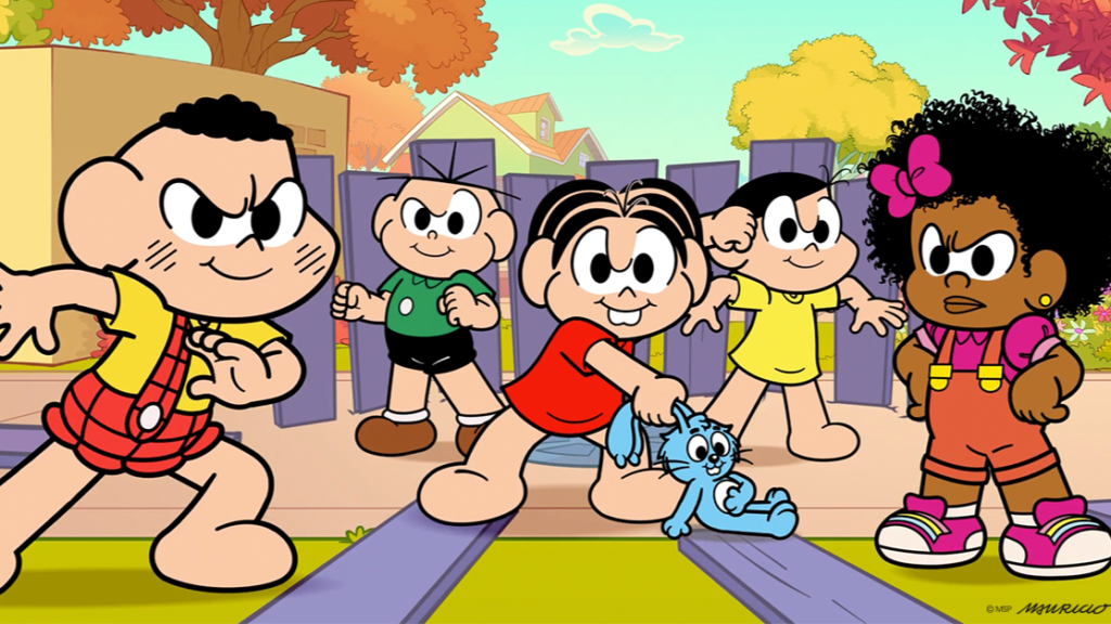 Texto alternativo: Cena de animação colorida da Turma da Mônica, em uma rua de bairro ensolarada com árvores de folhas alaranjadas e amarelas, casas ao fundo, céu azul com nuvens e uma cerca de tábuas roxas. Cinco crianças aparecem em pose de confronto, com expressões de determinação e sobrancelhas franzidas. Em primeiro plano, à esquerda, o Cebolinha, de cabelo preto e macacão xadrez vermelho sobre camiseta amarela, faz pose de luta. Atrás dele está o Cascão, de camiseta verde e short preto. No centro, a Mônica, de vestido vermelho e dentuça, segura pela orelha o coelhinho azul Sansão. Ao lado, a Magali, de vestido amarelo, ergue o punho. À direita, a Milena, menina negra de cabelos cacheados volumosos com laço rosa, macacão laranja e tênis rosa, está de braços na cintura e cenho franzido. No canto inferior direito aparecem a assinatura “Mauricio” e o crédito “© MSP”.