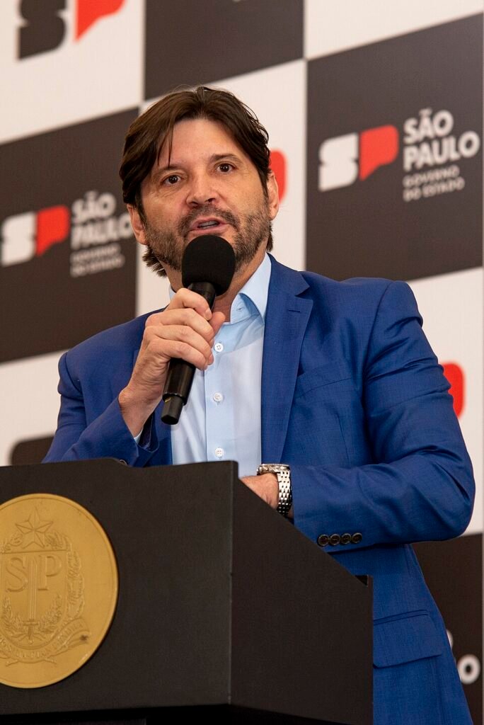 Homem branco de cabelo preto falando ao microfone