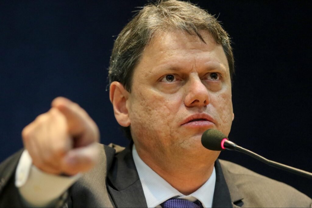 Homem branco falando ao microfone com o dedo apontado