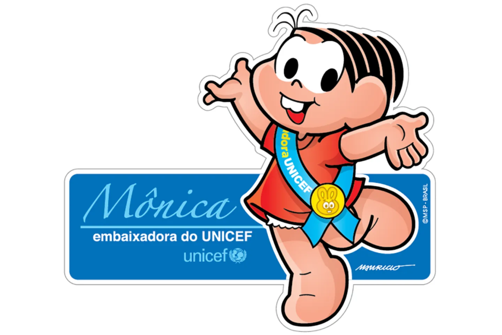 Arte em formato de adesivo, com contorno branco, mostrando a personagem Mônica em movimento alegre, com um pé erguido e os braços abertos, sorrindo e mostrando os dentes da frente. Ela veste vestido vermelho e usa uma faixa azul-clara de lado a lado, com a palavra “UNICEF” e uma medalha dourada com um coelhinho. Atrás dela há uma placa azul retangular com o nome “Mônica” em letra cursiva azul-clara, o texto “embaixadora do UNICEF” em branco e o logotipo do UNICEF. Nos cantos aparecem a assinatura “Mauricio” e o crédito “© MSP - Brasil”.