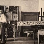 Foto de fotografia em preto e branco do artista surrealista Joan Miró em seu ateliê de arte cercado por telas e esboços.