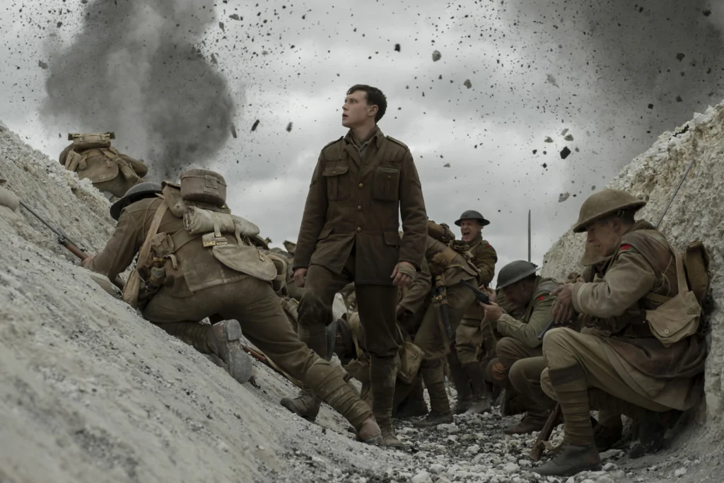 Cena do filme 1917. Um grupo de homens está vestido em roupas militares em uma trincheira, com destaque para um, ao centro e em pé.