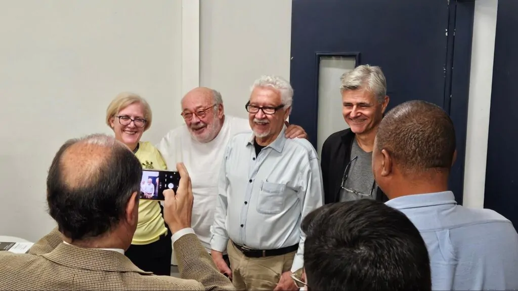 Mulher vestida de amarelo tira foto ao lado de três homens, todos em pé.
