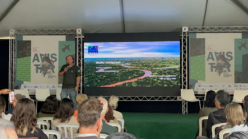 Palestra de Rodrigo Agostinho, ao fundo, apresentando um slide, e plateia com cadeiras de plástico