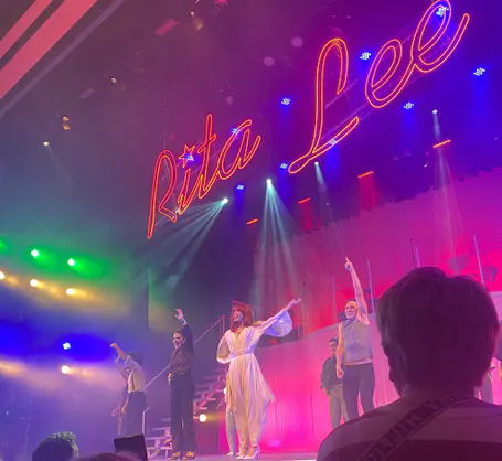 Mel Lisboa e outros atores do musical contracenando no palco. Em cima deles, um letreiro com o escrito "Rita Lee"