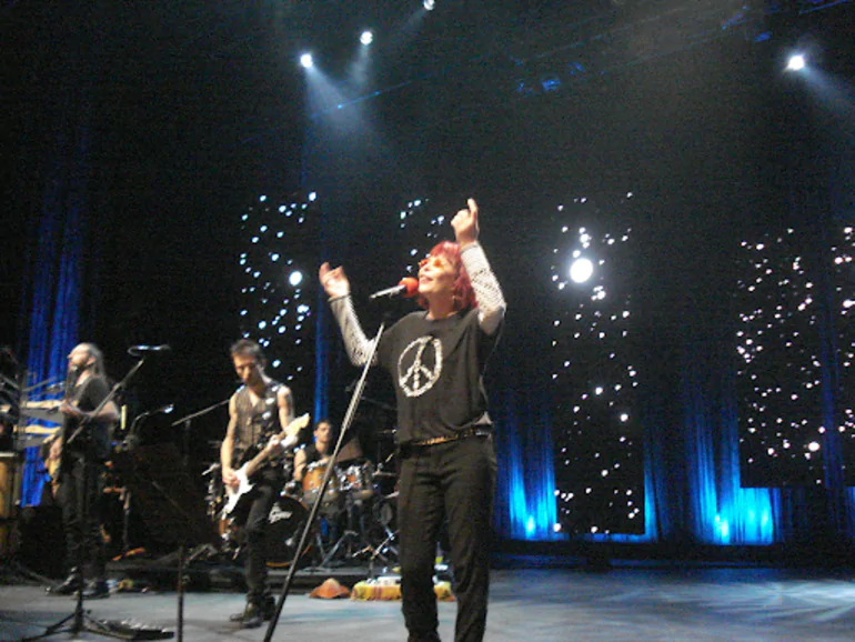 Rita Lee cantando em show com roupa que contém o símbolo da paz estampado
