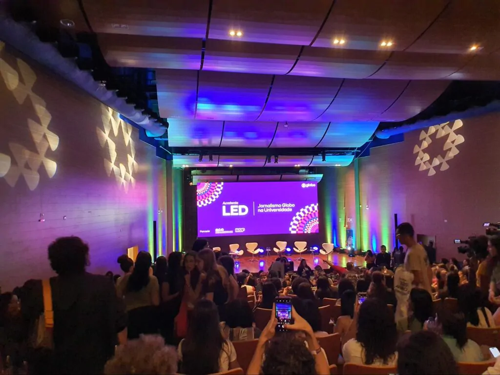 auditório com diversas pessoas, em maioria estudantes, aguardando para acompanhar uma aula de jornalistas reconhecidos em todo o Brasil