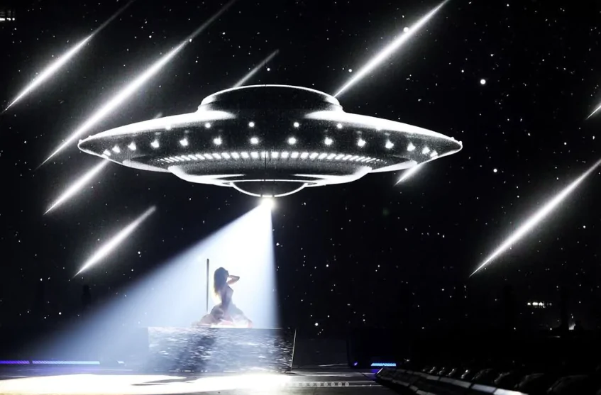 Taylor Swift aparece ajoelhada, de lado para quem tirou a foto. Ela é iluminada por uma luz, vinda de uma nave alienígena, acompanhada por feixes de luz. O fundo é escuro.