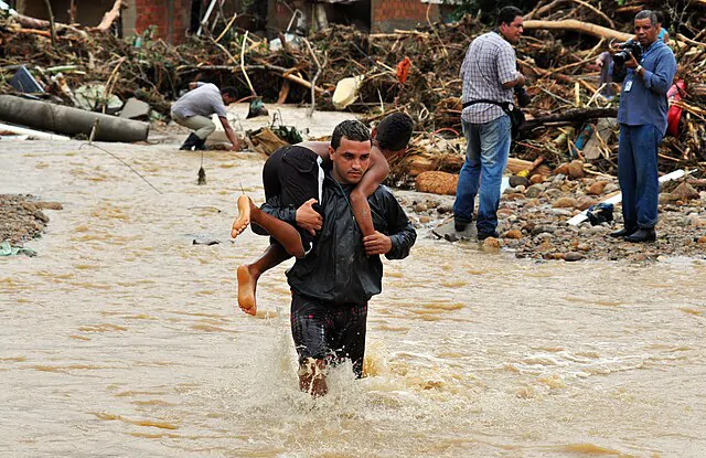 Homem carregando criança nas costas pare retirá-la de uma enchente, evento influenciado para mudanças climáticas
