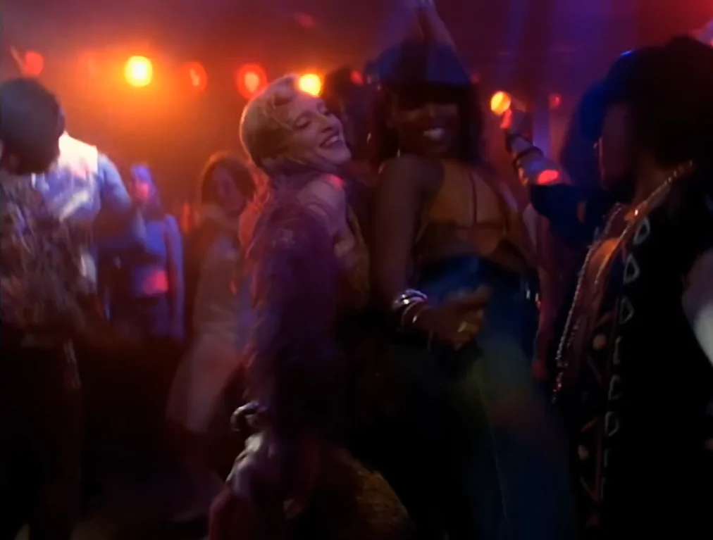 Madonna dança ao lado de outras pessoas em seu clipe. As cores são escuras e avermelhadas. 