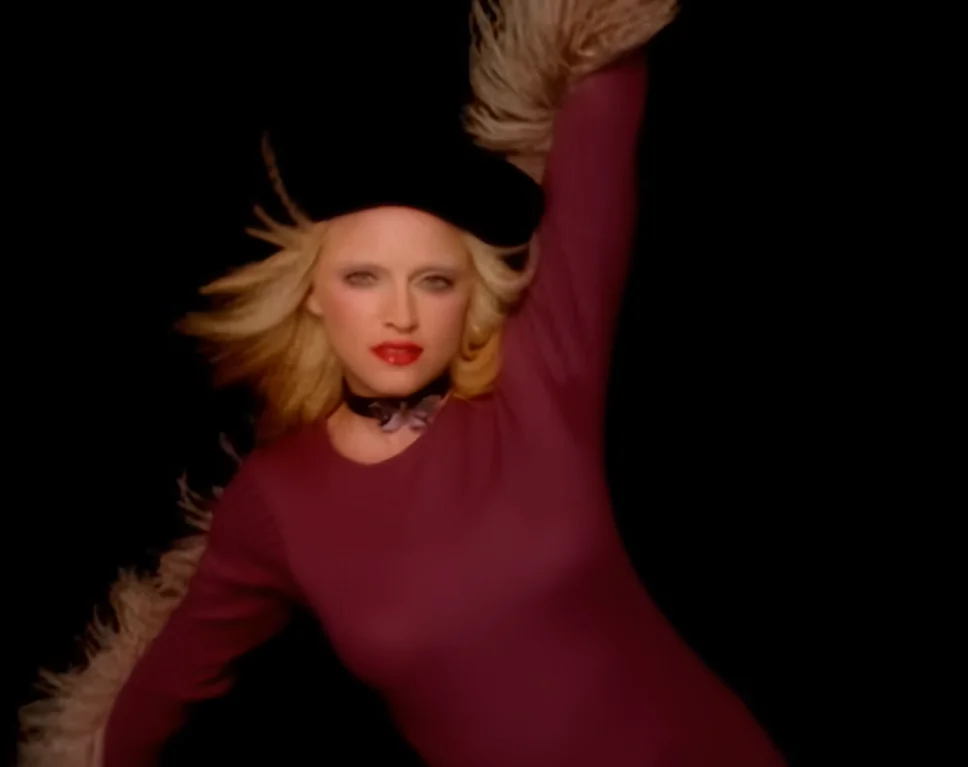 Madonna posa para foto. Ela usa um vestido justo na cor bordô, batom vermelho e uma boina preta. 