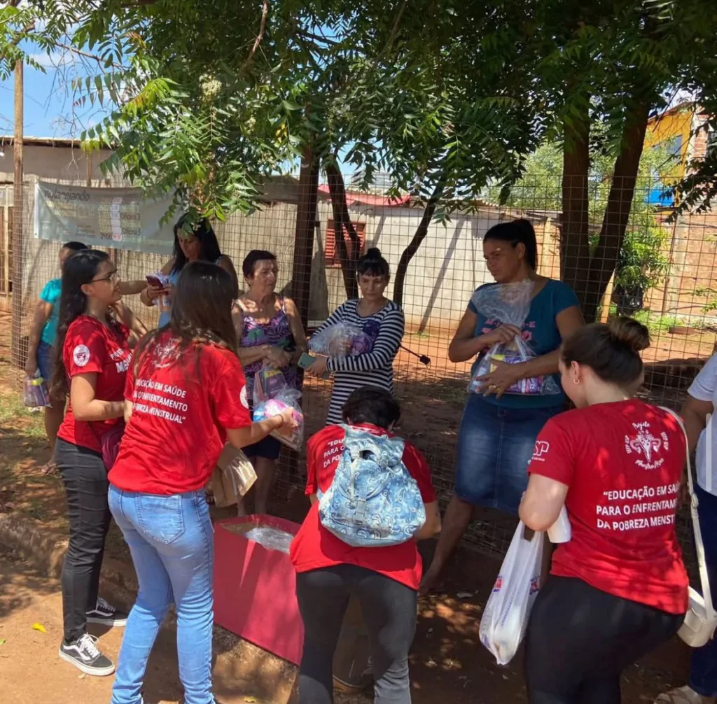 Imagem de várias pessoas com camista vermelha distribuindo kits de higienene