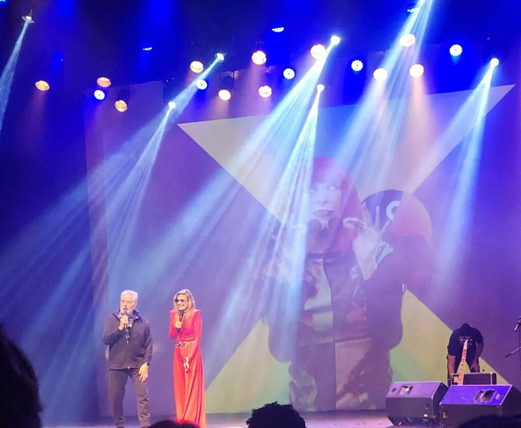 Luisa Mel e Roberto de Carvalho no palco do Prêmio Papagaio, com imagem de Rita Lee ao fundo