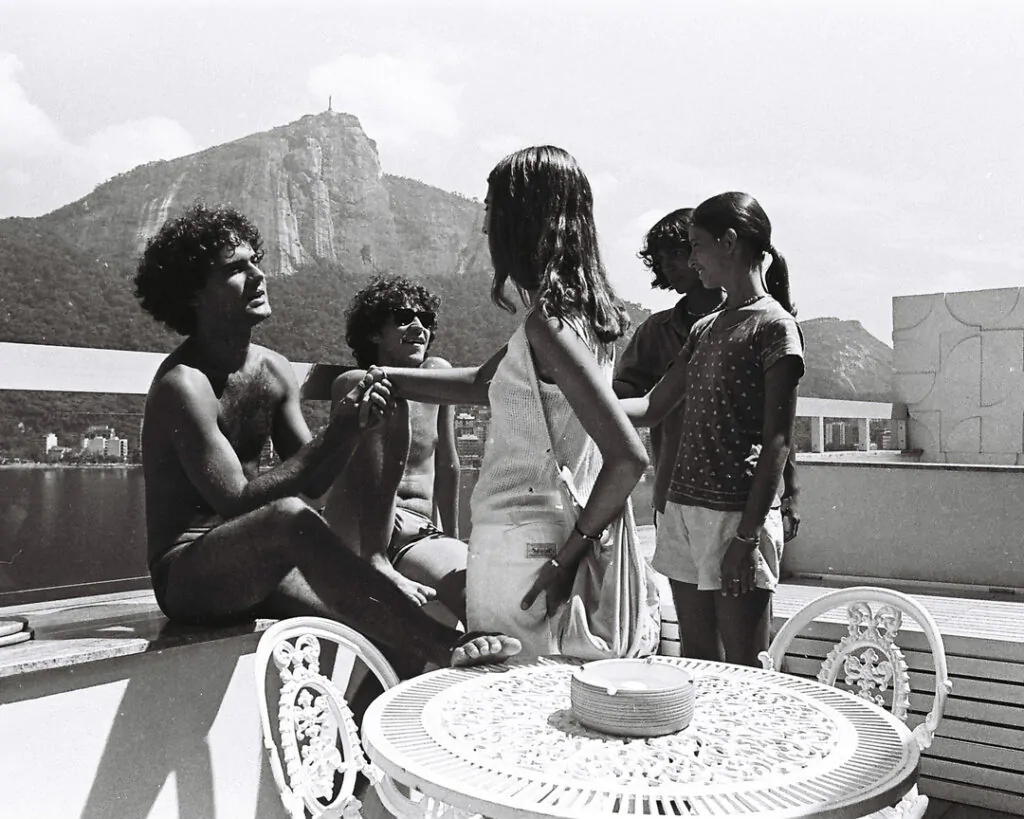 Cazuza na juventude, ao lago de amigos. Ele está sentado em uma mureta e a fotografia está em preto e branco.